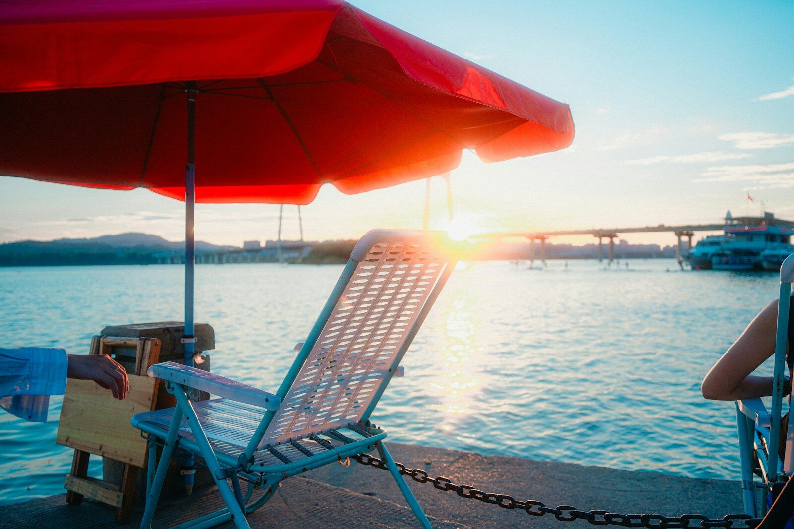 Red umbrella and chairs by water at sunset